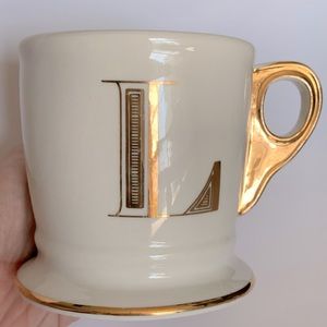 Anthropology coffee mug, personalized “L” gold lettering, cup is white.